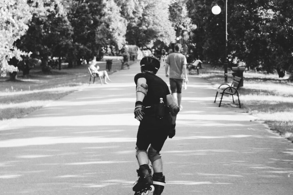 Black and white photo of a person rollerblading on a park path, captured in motion.